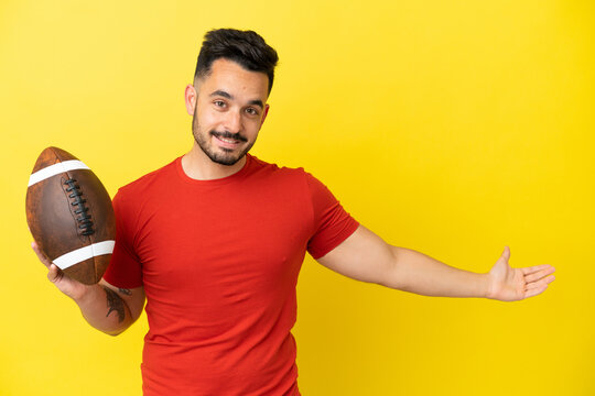 Young Caucasian man playing rugby isolated on yellow background extending hands to the side for inviting to come
