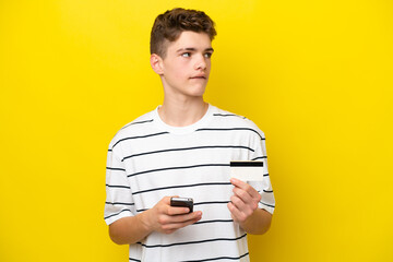 Teenager Russian man isolated on yellow background buying with the mobile with a credit card while...