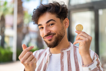 Handsome Arab man at outdoors holding a Bitcoin
