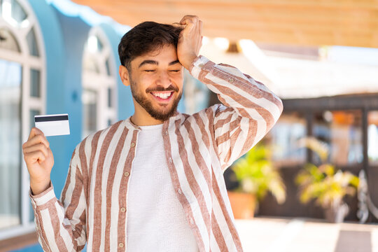Fototapeta Handsome Arab man holding a credit card at outdoors has realized something and intending the solution