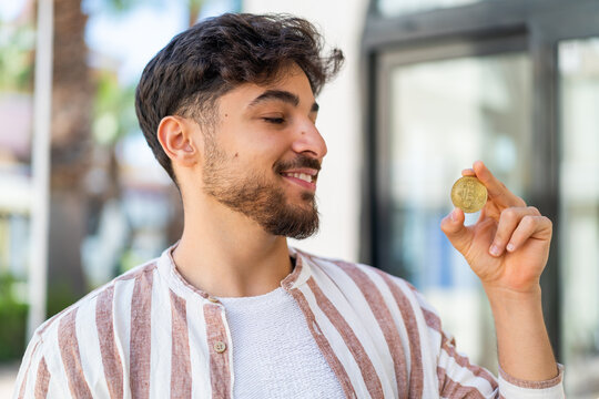 Fototapeta Handsome Arab man holding a Bitcoin at outdoors with happy expression