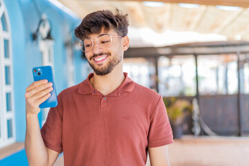 Young Arabian handsome man using mobile phone at outdoors with happy expression