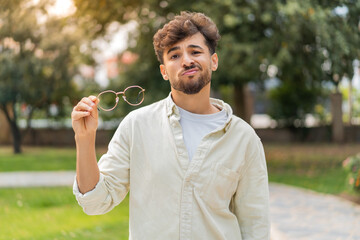 Young Arabian handsome man with glasses at outdoors with sad expression