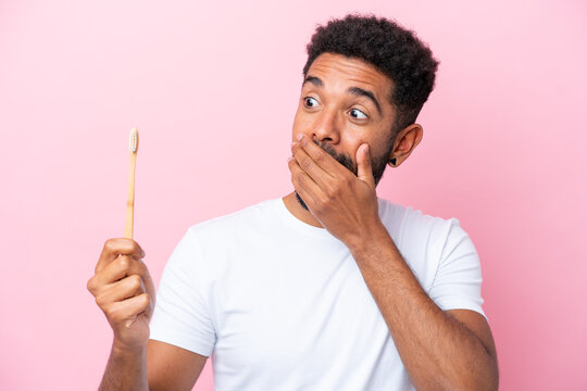 Young Brazilian man brushing teeth isolated on pink background with surprise and shocked facial expression - Powered by Adobe