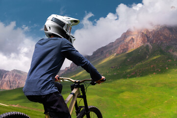 Man sits on a bicycle in a green field with mountains in the background. Concept of mountain biking and outdoor training