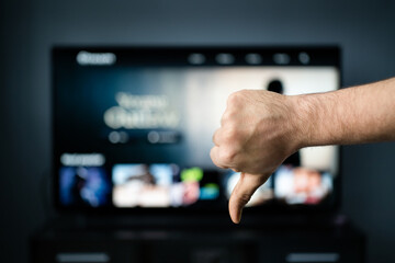 Bad movie. Film critic watching tv. Thumbs down, dislike. Stream service. Cancel subscription. Negative feedback. Video on demand, VOD. Television series and film site online with expensive price.
