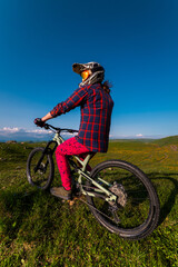 vertical photograph of an unrecognizable man sitting on a bicycle in full-face protective gear against a backdrop of mountains. Concept for mountain biking and outdoor training