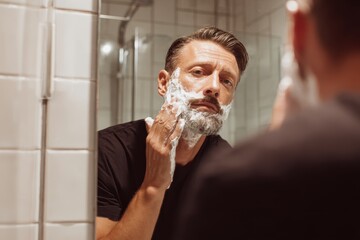 Man in bathroom applying shaving cream looking in mirror ready to shave