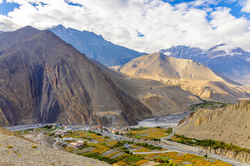 Aerial view of the Upper Mustang valley in Jomsom, Nepal, featuring rugged mountains, a small village, and golden fields under a bright sky. A stunning scene of Himalayan landscape and remote beauty.