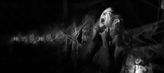 Terrified woman screaming while tearing spiderweb with hands, expression of fear and despair on...