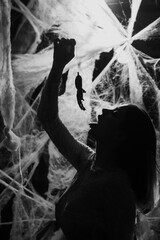 halloween, decoration and horror. Silhouette of woman holding big spider standing in spider web. black and white photo