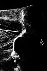 Fine art photo of a young woman wrapped in spider web on black background. Black and white photo.