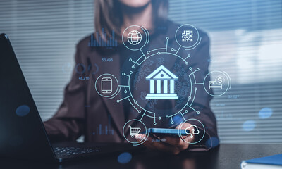 Digital banking concept with finance icons and hologram interface on screen held by businesswoman in modern office environment with laptop setup.