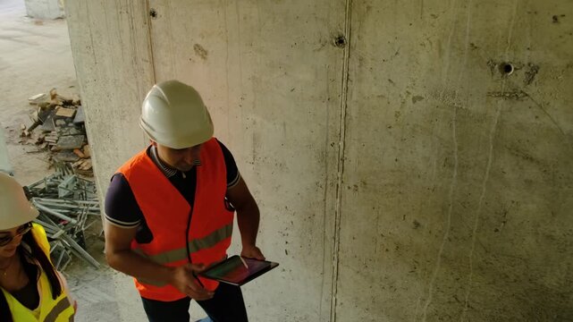 Worker and engineer climb steps assessing work area. Builder holds tablet with floor plan explaining features of structures and systems to colleague