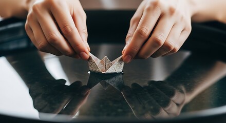 Hands Gently Guiding Paper Boat on Water, Reflective Surface, Artistic Composition.