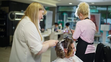 Hairdresser team with assistant applying hair dye in salon showing beauty treatment hairstyle coloring process and professional care for feminine transformation
