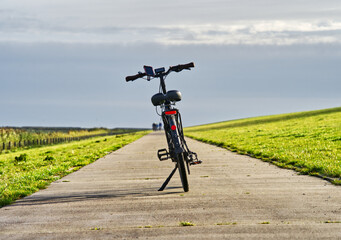 E-bike resting on a concrete path along a grassy dike near the north sea in carolinensiel, germany