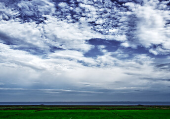 Dark clouds gathering over vast green marshland meeting the tranquil north sea horizon under an evolving sky