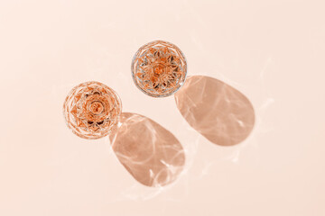 Minimal style glasses of rose wine or champagne on pastel pink with shadows and light reflection. Bright shiny wineglass with sparkling alcohol drink at sunlight, aesthetic lifestyle summer beverage