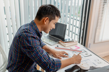 A young male architect is working with blueprints at his desk, using rulers and drawing tools to refine details. He appears focused and engaged, balancing creativity with precision.