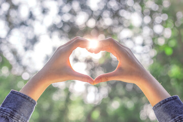Sun shines through the hands symbolically form a heart on nature bokeh background