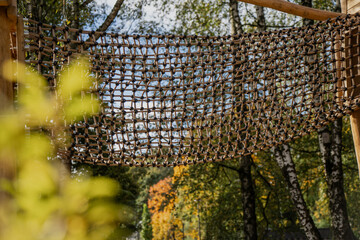 Rope climbing bridge net made of durable synthetic rope and wooden frame installed in outdoor playground providing safe adventure structure for balance coordination and recreation