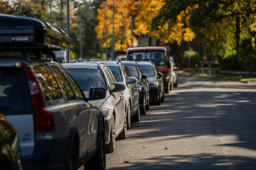 Row of parked cars along residential street with autumn foliage, including vehicle equipped with roof cargo box, showcasing urban transportation and suburban parking environment