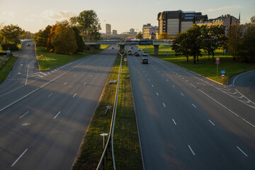 Wide highway in Riga with light evening traffic leading toward city center, divided lanes and modern infrastructure under warm sunset light showing balanced urban composition