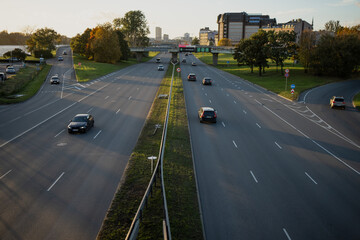 Riga city highway with moderate evening traffic and divided lanes leading toward skyline, modern urban infrastructure captured under warm sunset light with clear road perspective