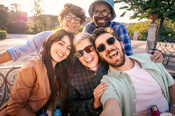 Fototapeta premium Happy group of diverse friends taking a selfie in a park at sunset. Authentic moment of friendship, travel and youth lifestyle.