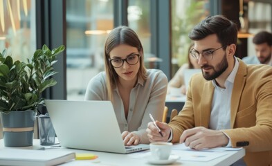 Two professionals working together in a modern office, focused on a laptop and documents, planning business strategies.