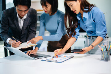 Asian business team brainstorming and discussing data charts in office, showing teamwork, planning, and collaboration