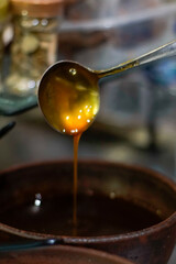 Close-up of liquid palm sugar (gula aren/kinca) being poured from a metal ladle into a rustic earthenware bowl. Warm amber syrup with glossy texture and artisanal kitchen background