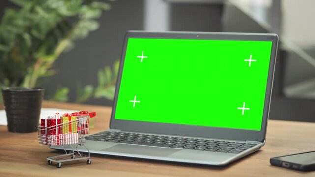 laptop green screen on wooden table desk,3d christmas shopping cart full of gifts,online purchase e-commerce concept