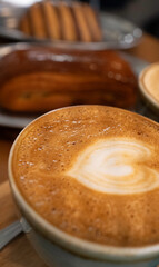 Coffee cup displaying a heart in milk foam with blurred pastries in the background