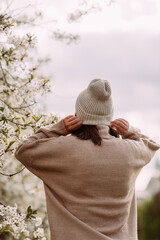 A woman in a sweater and hat against a backdrop of blossoming trees 7279.