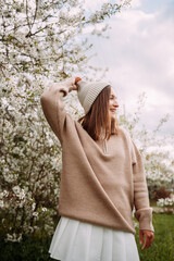 A girl in a light sweater and white skirt against a backdrop of blossoming trees 7282.
