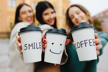 Three smiling women enjoying takeaway coffee with positive messages in autumn