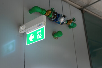 Fire escape route exit sign, lighting banner is glowing in green light that installed at building interior. Transportation sign object.