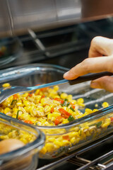 Close-up of stir-fried corn with sliced red and green chili being mixed with a spoon in a glass container, traditional Indonesian homemade dish.