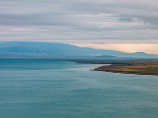 The shoreline of Qinghai Lake features turquoise waters meeting grasslands under misty mountains and cloudy skies, showcasing a serene plateau lake landscape.
