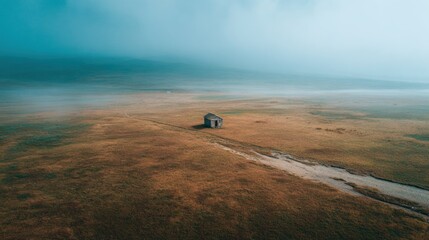 A lone, weathered cabin sits in a vast, grassy plain shrouded in low-lying fog
