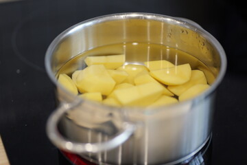 Stainless steel pot with water boiling on a red stovetop. Food ingredients are visible inside the pot: Plze?, Czech - Oct,11,2025