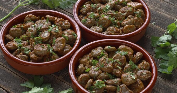 Three tapas bowls with a vegan version of Spanish habas con jam&oacute;n - broad beans with second skin cooked with olive oil, garlic, onions, smoked paprika, and white wine. Rustic wooden table.
