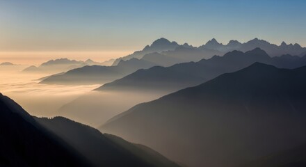 A misty mountain range with a golden sunrise, silhouetted against a clear sky.