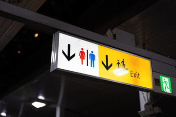 Toilet and exit lighting information signboard at public train station with arrow sign. Sign for transportation equipment object, close-up.