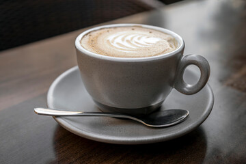 Cappuccino with latte art in ceramic cup on saucer