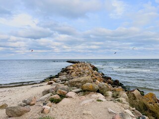 Rocky pier stretching into calm sea under cloudy sky, peaceful coastal landscape with gentle waves

