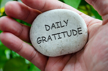 Hand holding a white stone with DAILY GRATITUDE text engraved on it, symbolizing life purpose and appreciation for everyday blessings.