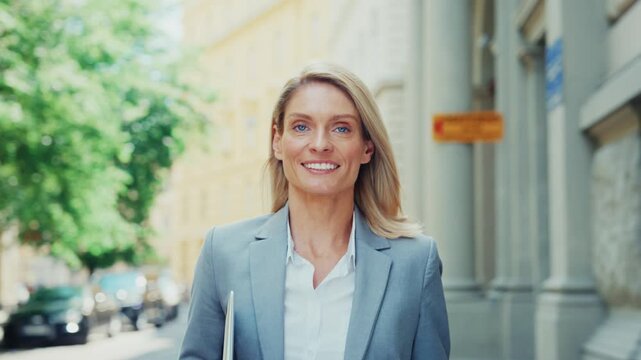 Smiling Businesswoman Walking Outdoors Holding Laptop in City